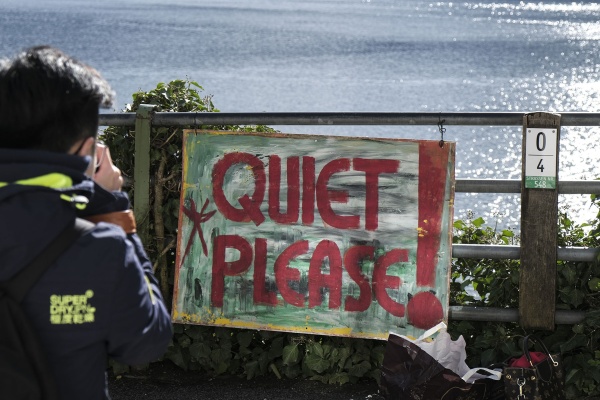 Ein Tourist nimmt konzentriert ein Foto von Hallstatt auf, zu sehen ist auch ein selbst gemachtes Schild, dass die TouristInnen auffordert leise zu sein.