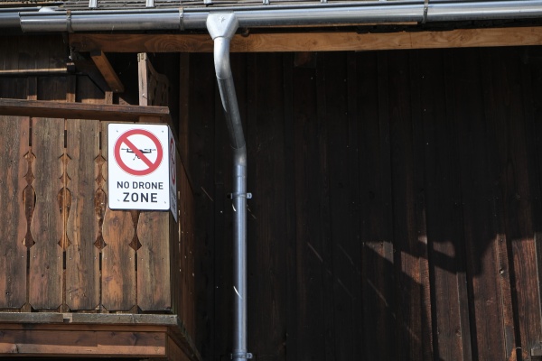 An einer Holzwand, neben einer Regenrinne hängt eines der omnipräsenten Schilder, die TouristInnen darauf hinweist, dass Drohnen in Hallstatt verboten sind.